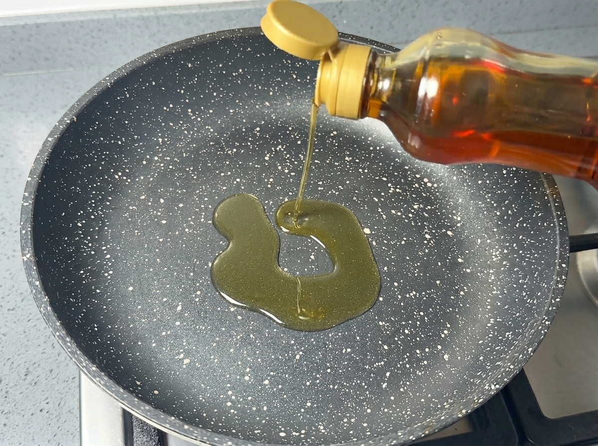 Speiseöl wird aus einer Flasche in eine dunkle, gesprenkelte beschichtete Pfanne gegossen.
