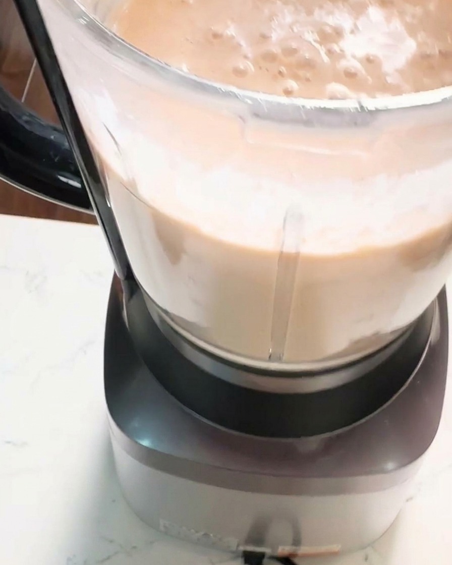 Nahaufnahme eines Mixbechers, in dem eine dicke, glatte und cremige orange-rosa Garnelenpaste verarbeitet wird.