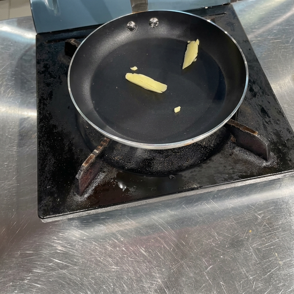 Ein kleines Stück gelbe Butter schmilzt in einer schwarzen, flachen Pfanne auf dem Herd.