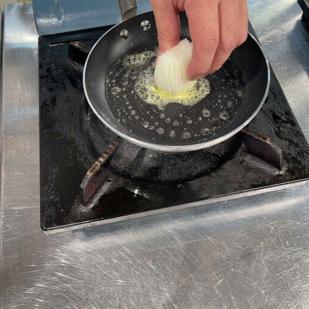 Eine Hand gibt eine Handvoll in Scheiben geschnittene weiße Zwiebeln in eine heiße Pfanne mit brodelnder, geschmolzener Butter.
