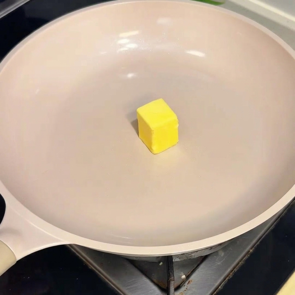 Ein Stück gelbe Butter schmilzt auf der Oberfläche einer heißen, cremefarbenen beschichteten Pfanne.