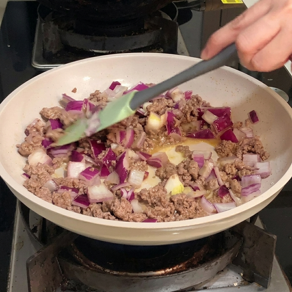 Gewürfelte rote Zwiebeln werden in einer Pfanne mit dem gebräunten Rinderhackfleisch vermengt.