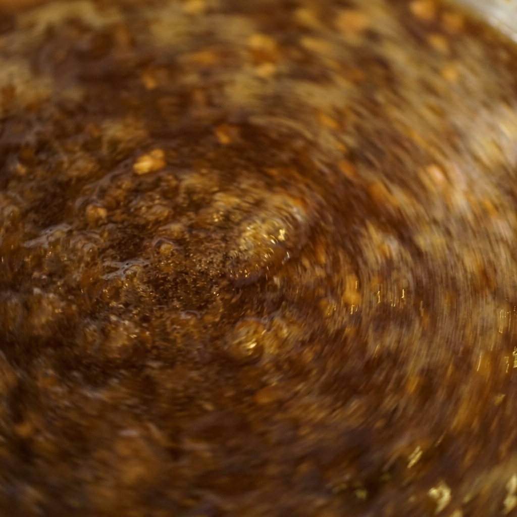Nahaufnahme einer dunkelbraunen Sauce, die unter ständigem Rühren kräftig in einem Topf sprudelt.