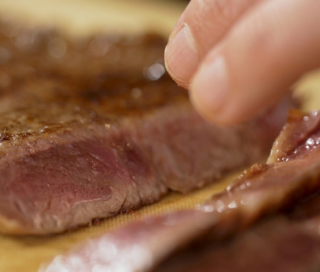 Eine Hand schneidet ein Stück gebratenes Rindfleisch auf einem Schneidebrett auf und gibt den perfekt rosa gegarten Kern frei.