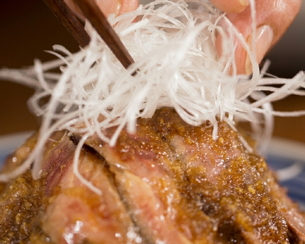 Stäbchen platzieren ein feines Nest aus weißen Lauchstreifen genau in der Mitte einer angerichteten Steak-Donburi-Bowl.