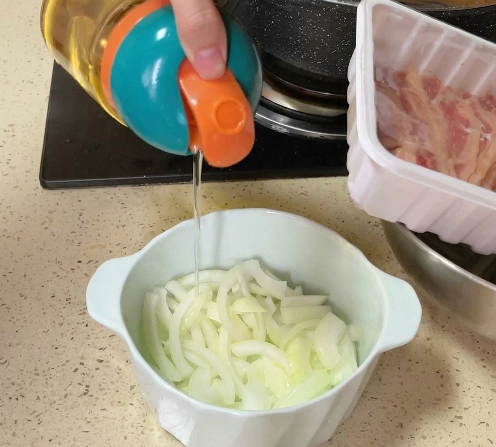 Ein bunter Spender gießt Öl oder Salz über eine Schüssel mit in Scheiben geschnittenen rohen Zwiebeln auf einer Küchenzeile.