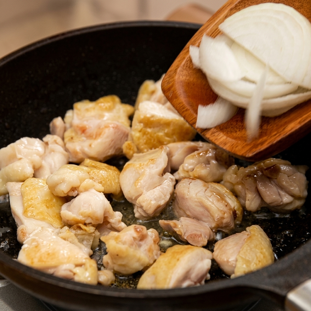 Fein geschnittene weiße Zwiebeln werden mit einem Holzspatel in die Pfanne zum angebratenen Hähnchenfleisch gegeben.