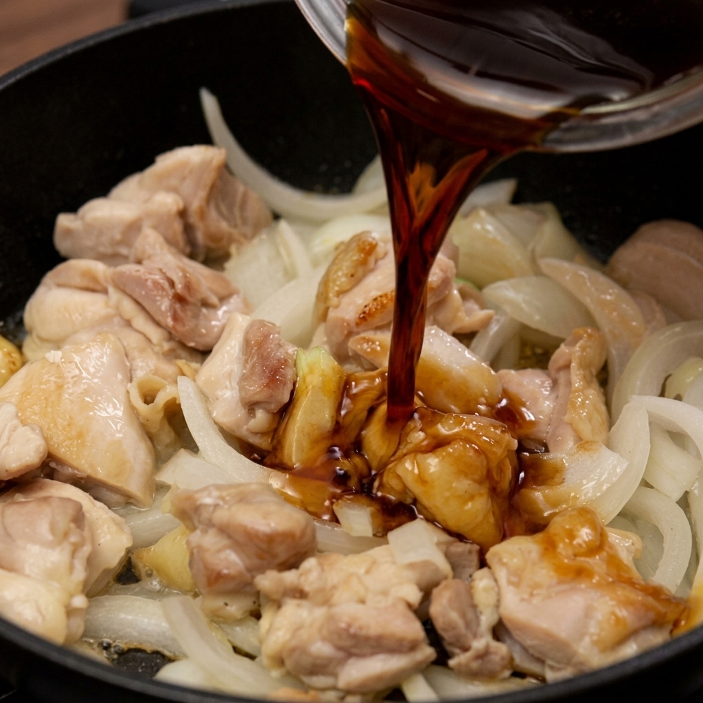 Eine dunkle Sauce auf Sojabasis wird in die Pfanne zu dem angebratenen Hähnchen und den Zwiebelstreifen gegossen.