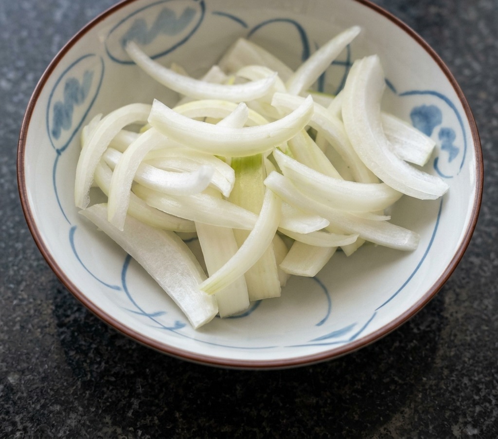 Eine weiße Keramikschüssel mit blauen Mustern, gefüllt mit frisch geschnittenen weißen Zwiebelspalten.