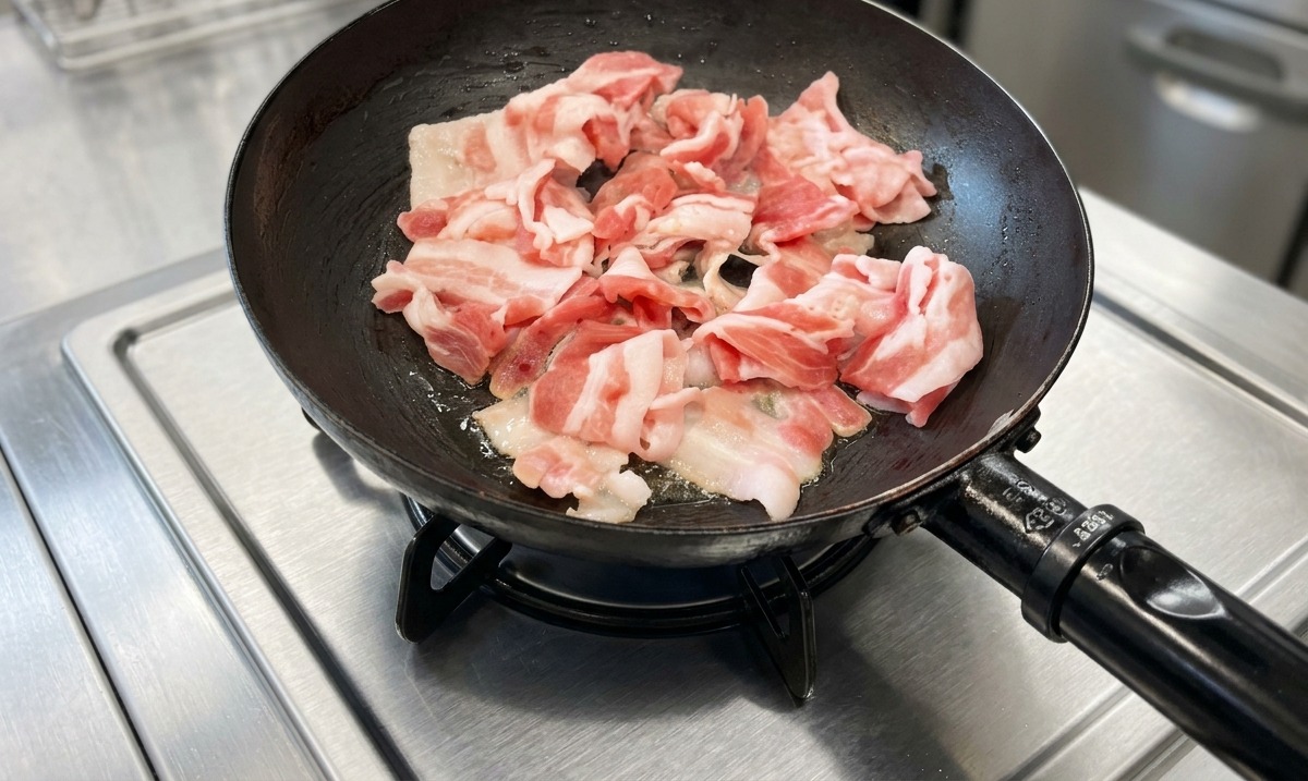 Schweinebauchscheiben werden in einer schwarzen Bratpfanne auf einem Edelstahlherd gebraten.