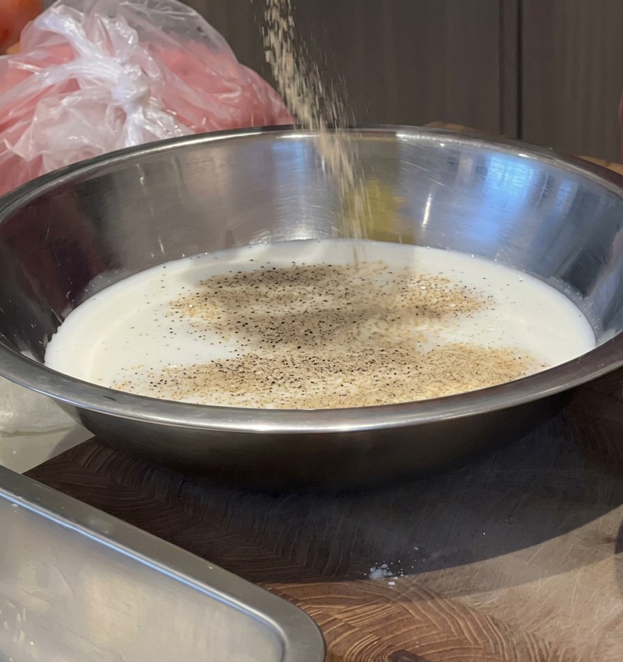 Eine Person gibt Gewürze aus einem Behälter in eine Silberschale mit Milch, um eine Marinade herzustellen.