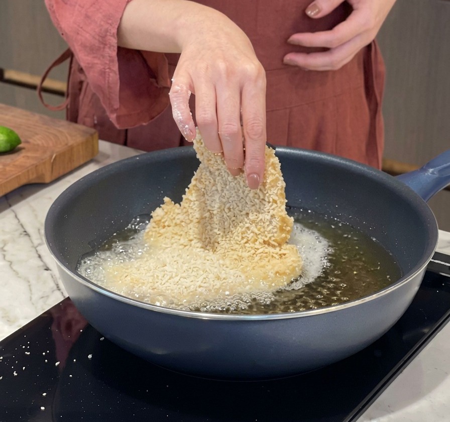 Eine Hand legt vorsichtig ein paniertes Schweineschnitzel in eine heiße Pfanne mit sprudelndem Öl.