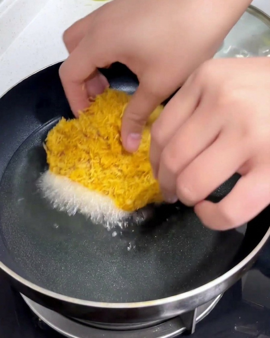 Ein paniertes Schweineschnitzel wird von Hand vorsichtig in eine Pfanne mit heißem, schimmerndem Öl gelegt.