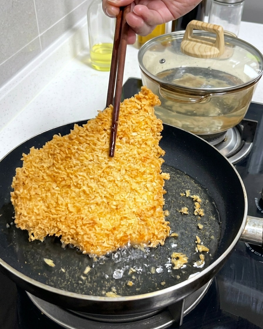 Ein großes, knuspriges, goldbraun paniertes Schweineschnitzel wird mit Holzstäbchen in einer Pfanne mit brodelndem Öl gewendet.