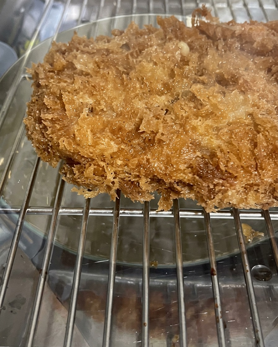 Nahaufnahme eines frittierten Schweineschnitzels mit einer knusprigen, unregelmäßigen Panko-Panade, das auf einem Kuchengitter ruht.
