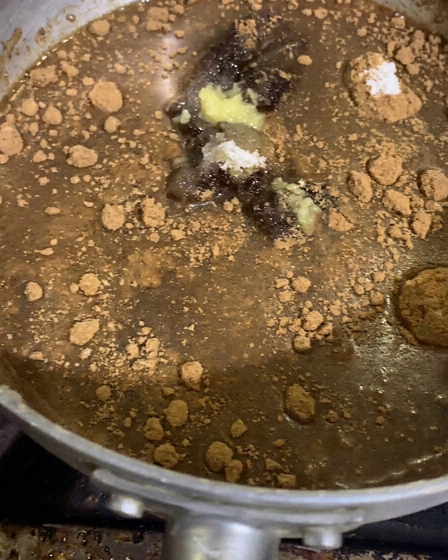 Kleine Häufchen aus gemahlenen Gewürzen, Knoblauch- und Ingwerpaste liegen vor dem Kochen auf einer dunklen Miso-Saucenbasis in einem silbernen Stieltopf.