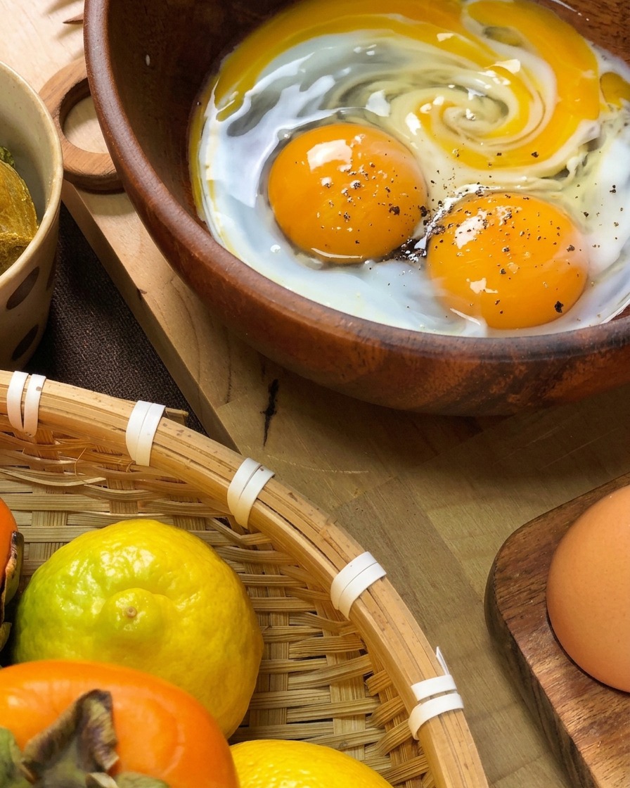 Frische Eier in einer Holzschale, gewürzt mit schwarzem Pfeffer und einem Schuss Milch, bereit zum Verquirlen.