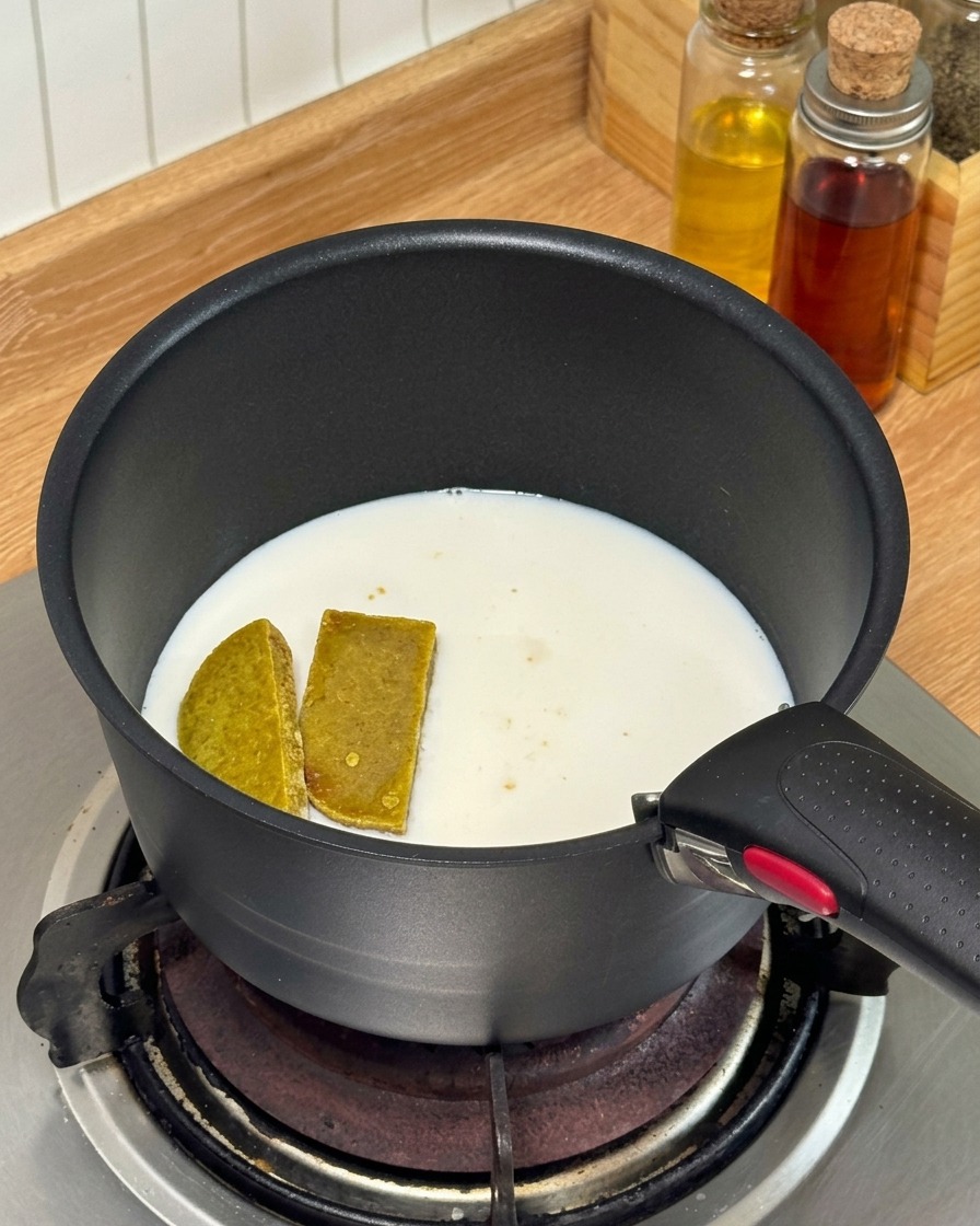 Curry-Würfel und Milch werden in einem kleinen schwarzen Stieltopf auf einem Gasherd erhitzt.