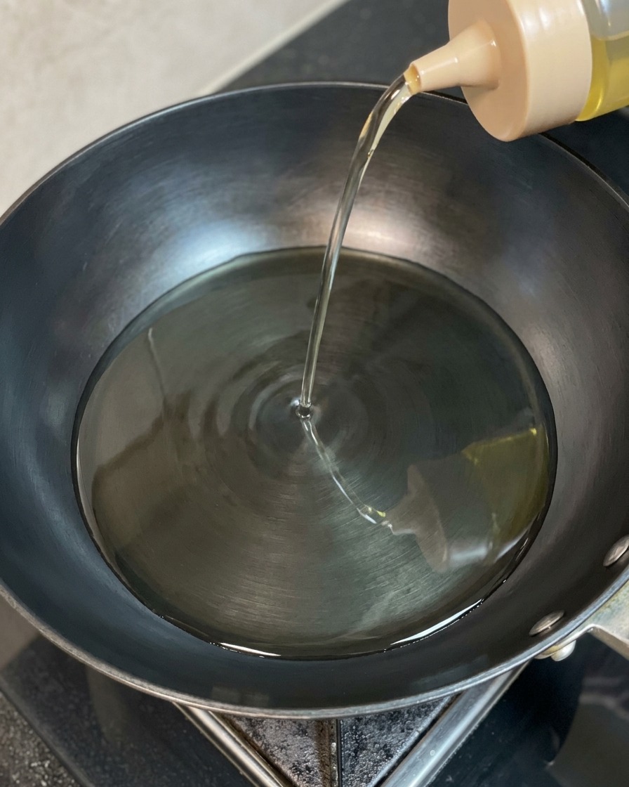 Klares Speiseöl wird aus einer Flasche in einen dunklen, erhitzten Wok gegossen.