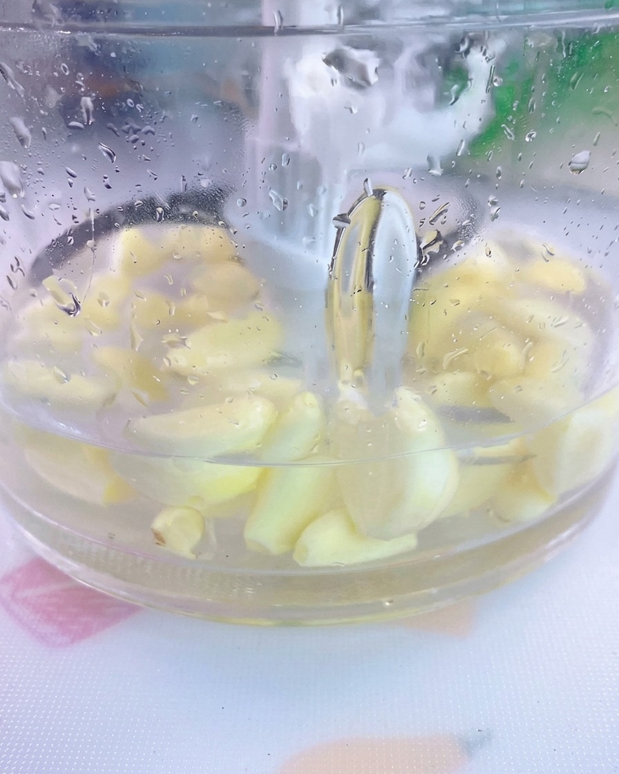 Geschälte Knoblauchzehen und Salz in Wasser in einem transparenten Mixer.