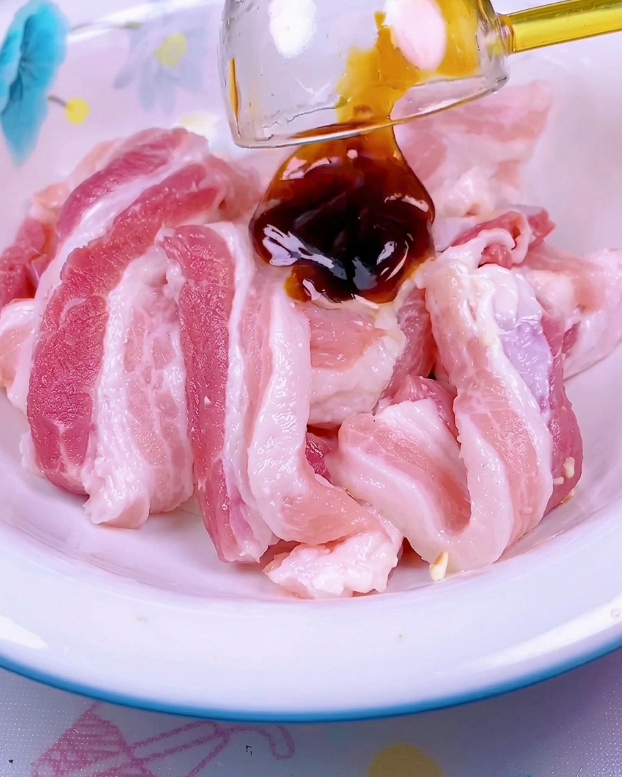 Dunkle rote Sauce wird über rohe Schweinebauchscheiben in einer weißen Schüssel geträufelt.