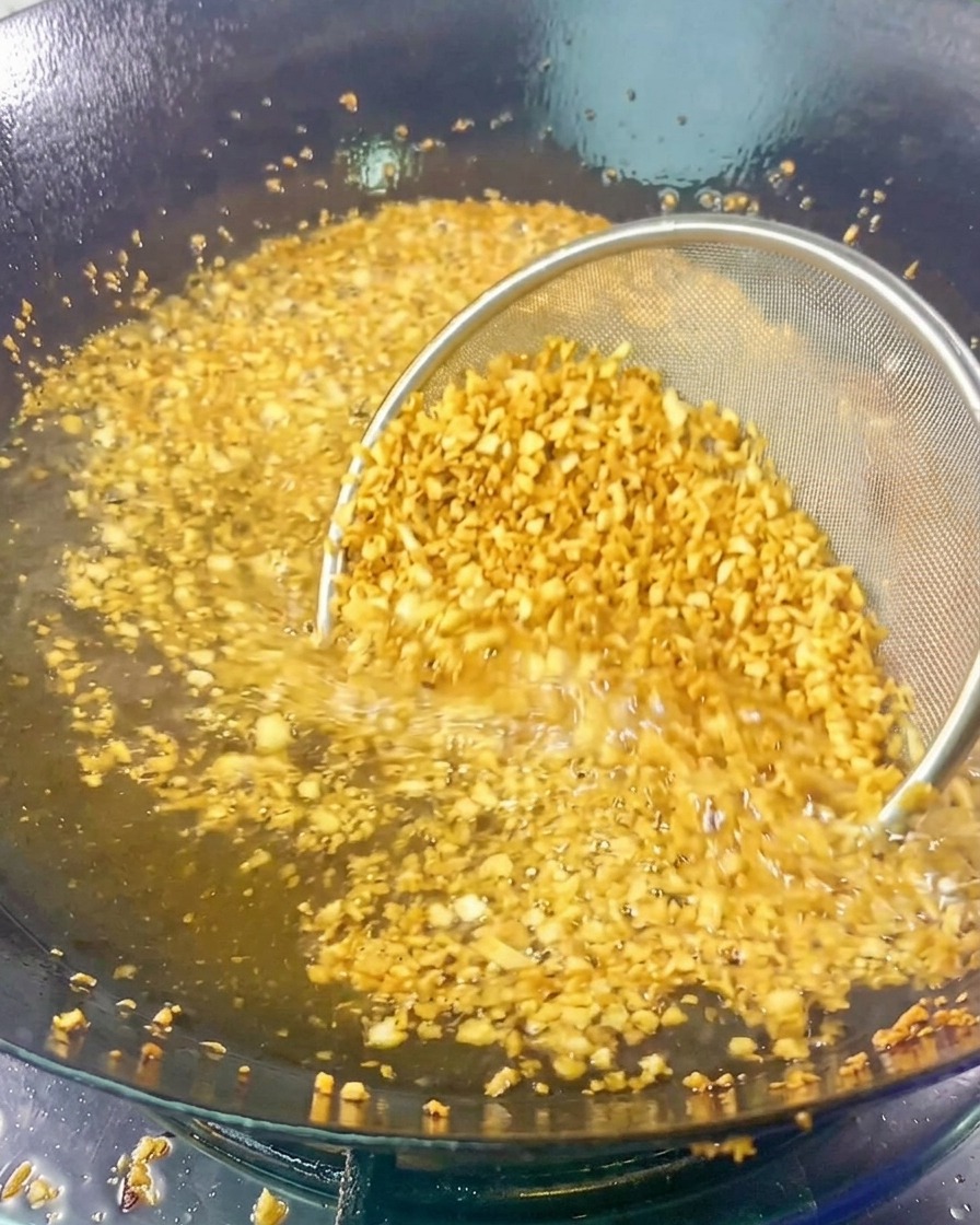 Ein feines Sieb mit gehacktem Knoblauch in heißem Öl, der goldgelb und aromatisch wird.