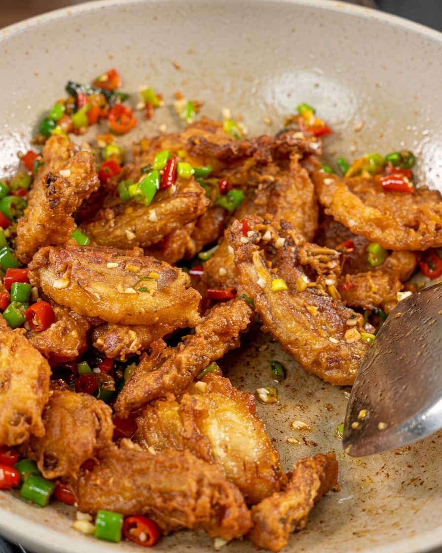 Nahaufnahme von knusprigem Schweinebauch, roter und grüner Paprika sowie Knoblauch im Wok, mit weißen Sesamsamen bestreut.