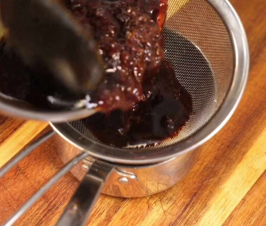 Dunkle Sauce wird durch ein feines Sieb gegossen, das die eingeweichten Bonitoflocken auffängt.