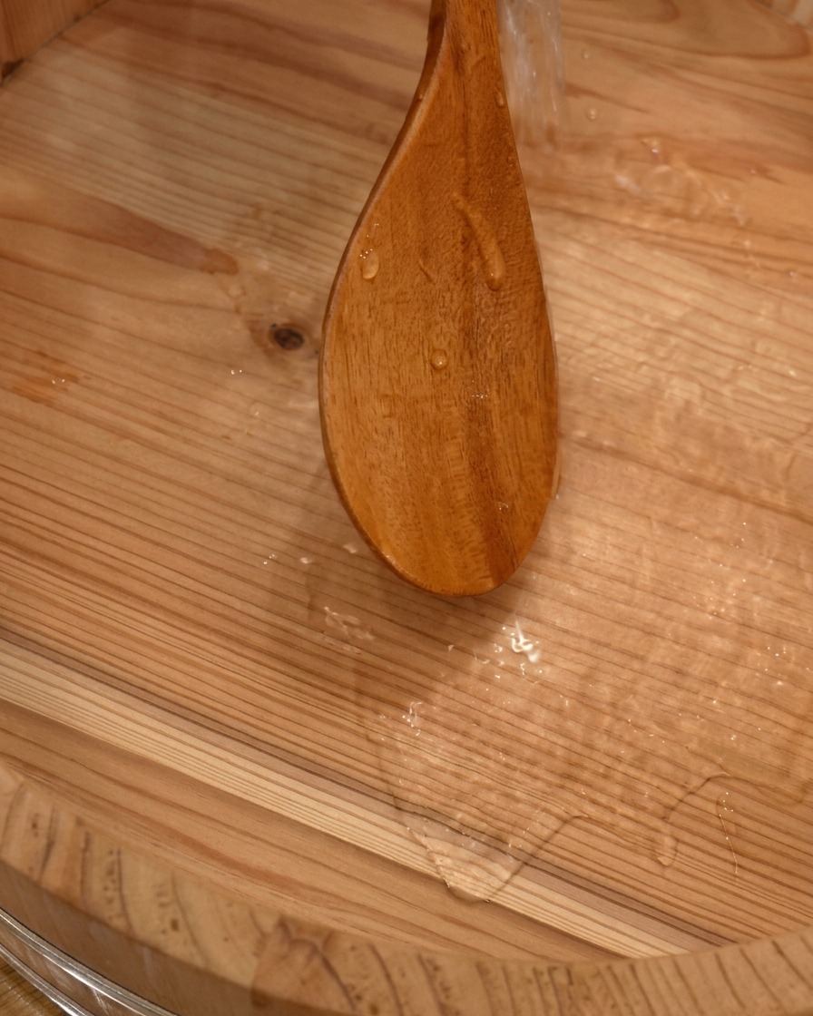 Wasser wird mit einem Holzlöffel in eine traditionelle, große Sushischale aus Holz gegossen.