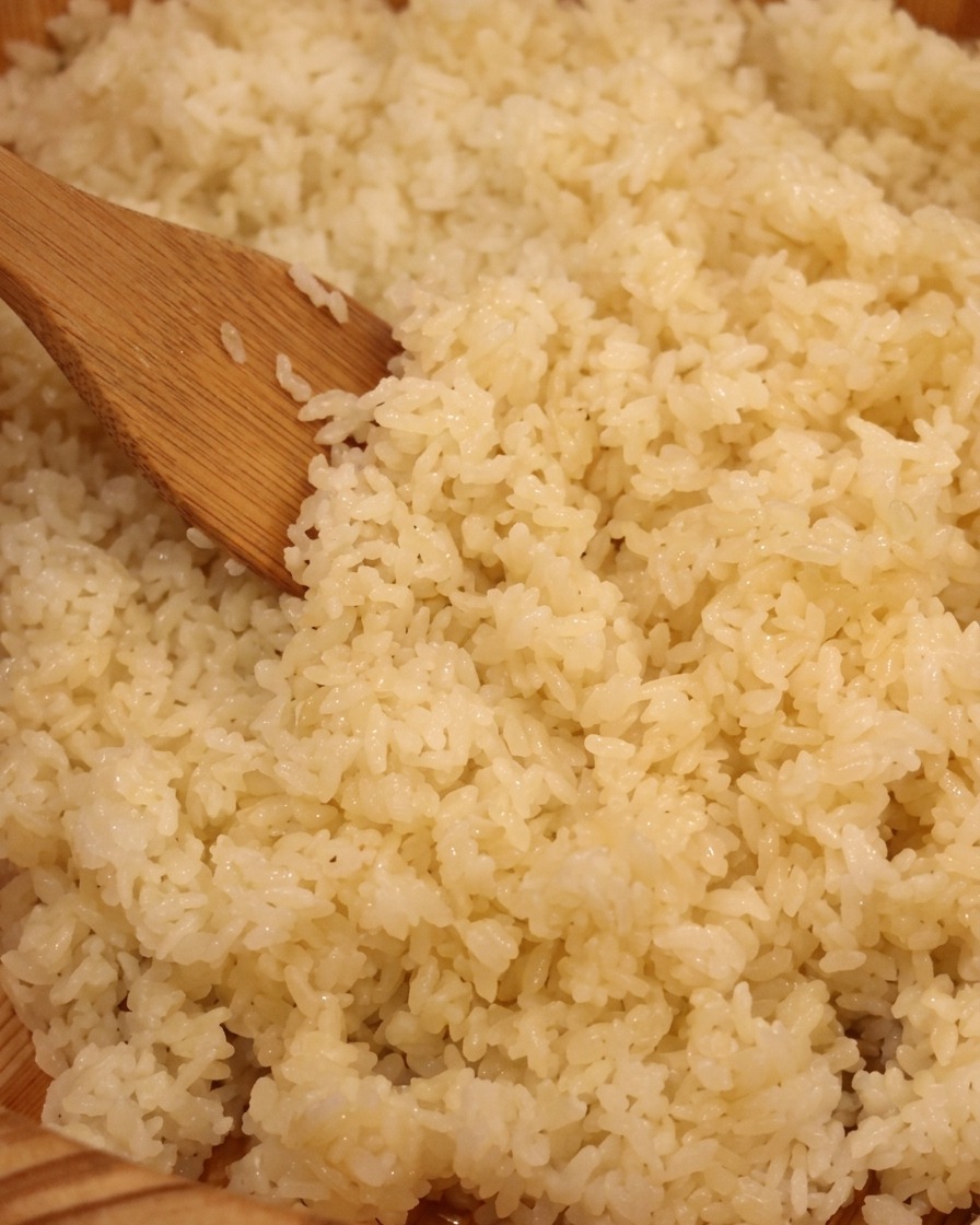 Eine Nahaufnahme eines Holzspatels, der gekochten weißen Reis in einer traditionellen hölzernen Sushischale mischt.