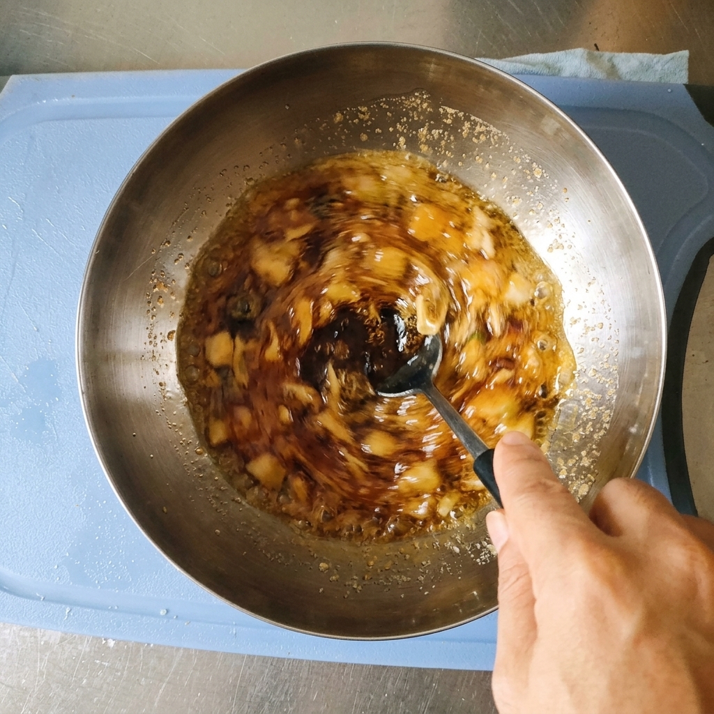 Eine Hand rührt eine dunkelbraune Marinade mit gehacktem Knoblauch und Frühlingszwiebeln mit einem Löffel in einer Edelstahlschüssel um.