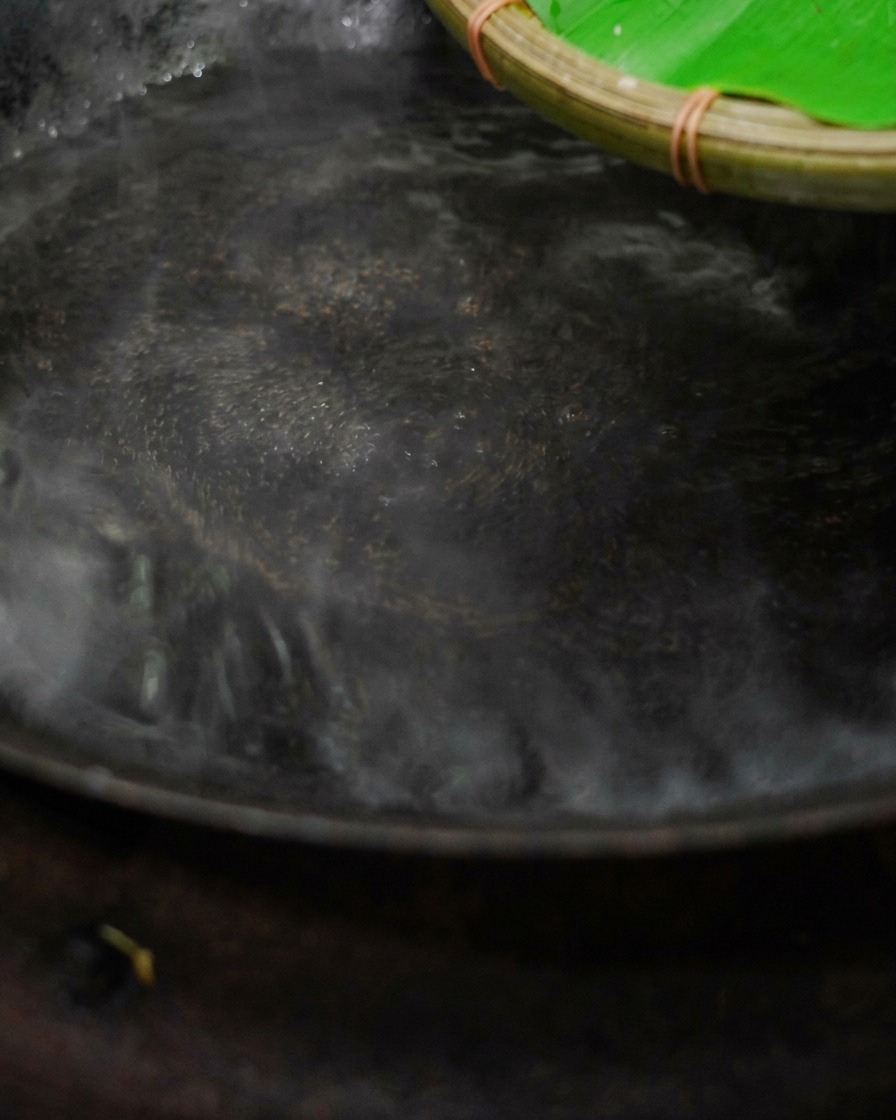Gehackte gepökelte Rippchen werden aus einem geflochtenen Bambuskorb in einen dampfenden Wok mit kochendem Wasser geschüttet.