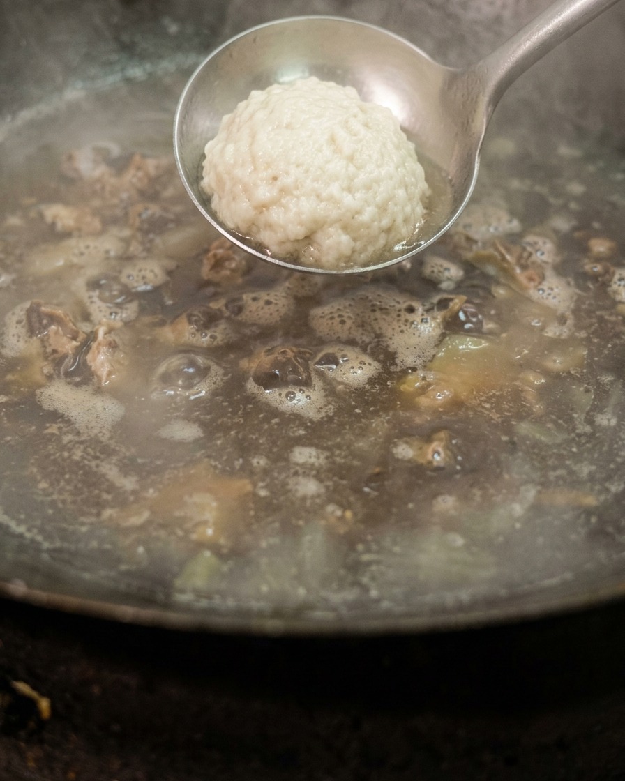 Eine Metallkelle mit weißem Salz wird in einen Wok mit kochendem Wasser und gepökeltem Fleisch abgesenkt.