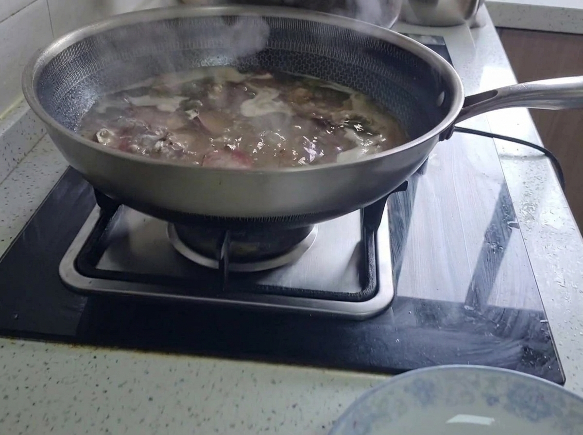 Gepökelte Schweinerippchen köcheln in einem großen Wok mit kochendem Wasser auf dem Küchenherd.