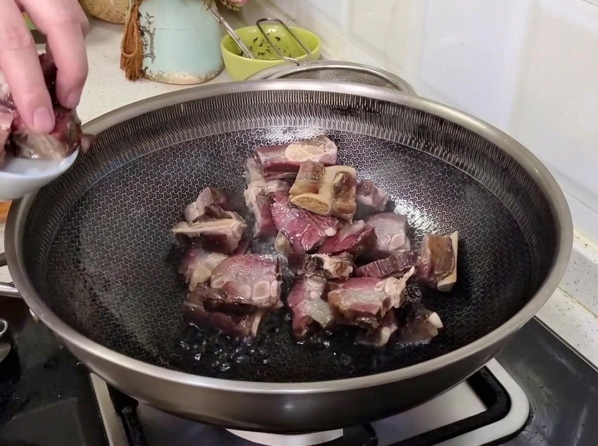 Eine Hand gibt die abgetropften gepökelten Schweinerippchen von einem kleinen Teller in einen heißen Wok zum Anbraten.