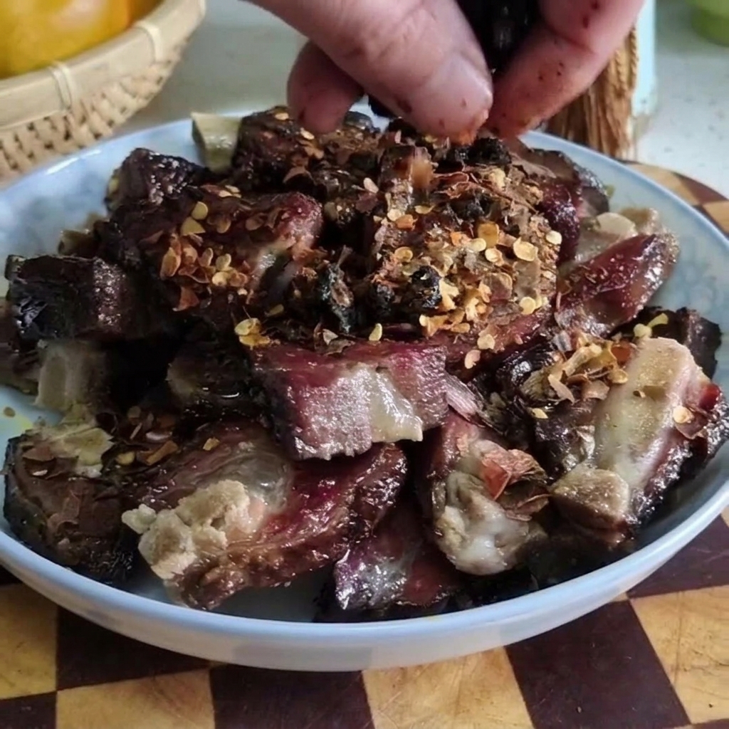 Nahaufnahme einer Hand, die fermentierte schwarze Bohnen über einen Teller mit gehackten gepökelten Schweinerippchen und Chiliflocken streut.