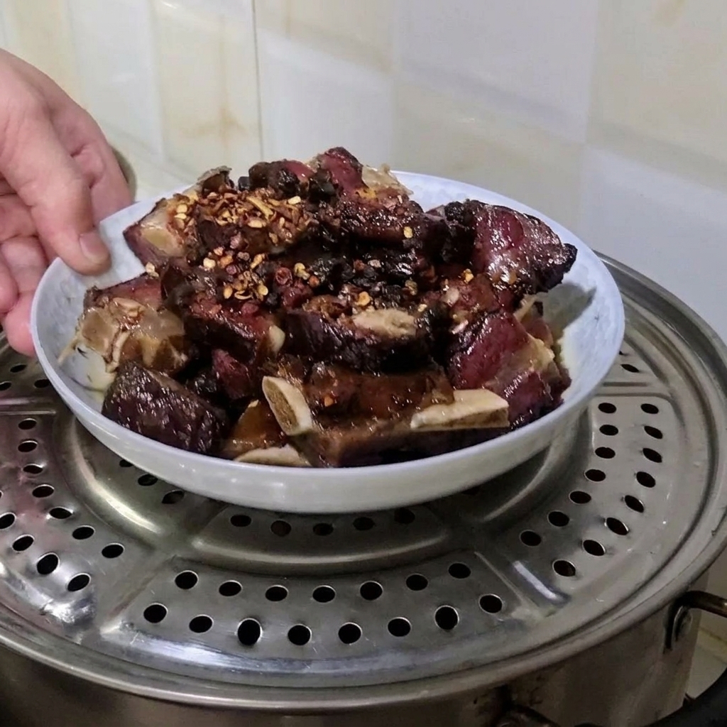 Eine Hand stellt einen teller mit gewürzten gepökelten Schweinerippchen auf einen Dämpfeinsatz aus Metall in einem Topf.