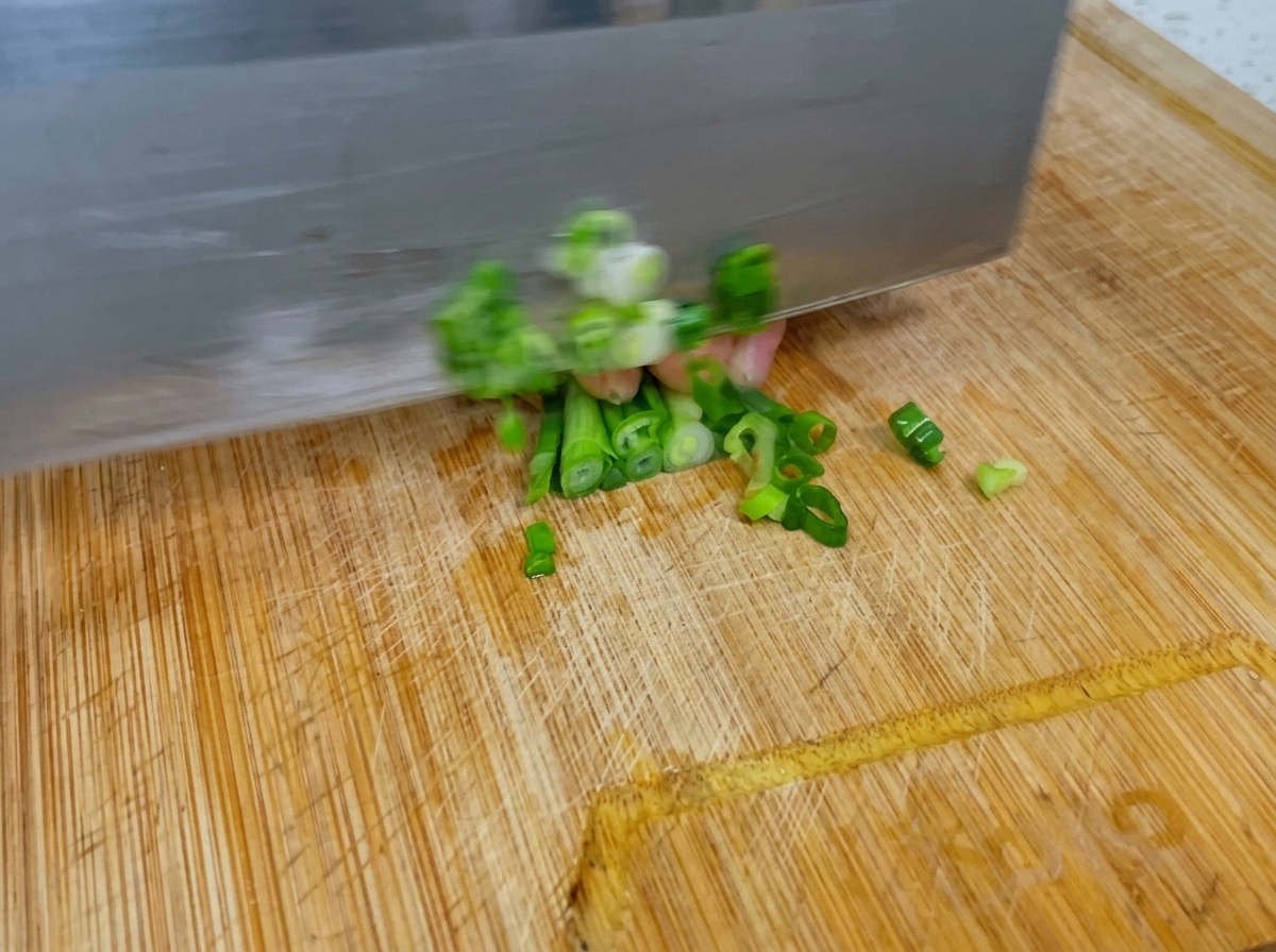 Ein Messer schneidet frische grüne Frühlingszwiebeln schnell auf einem Holzschneidebrett.