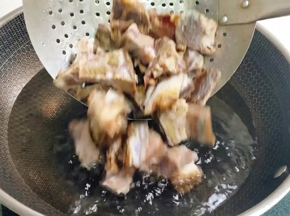 Gepökelte Schweinerippchen werden mit einem Schaumlöffel in einen mit kaltem Wasser gefüllten Wok gegeben.