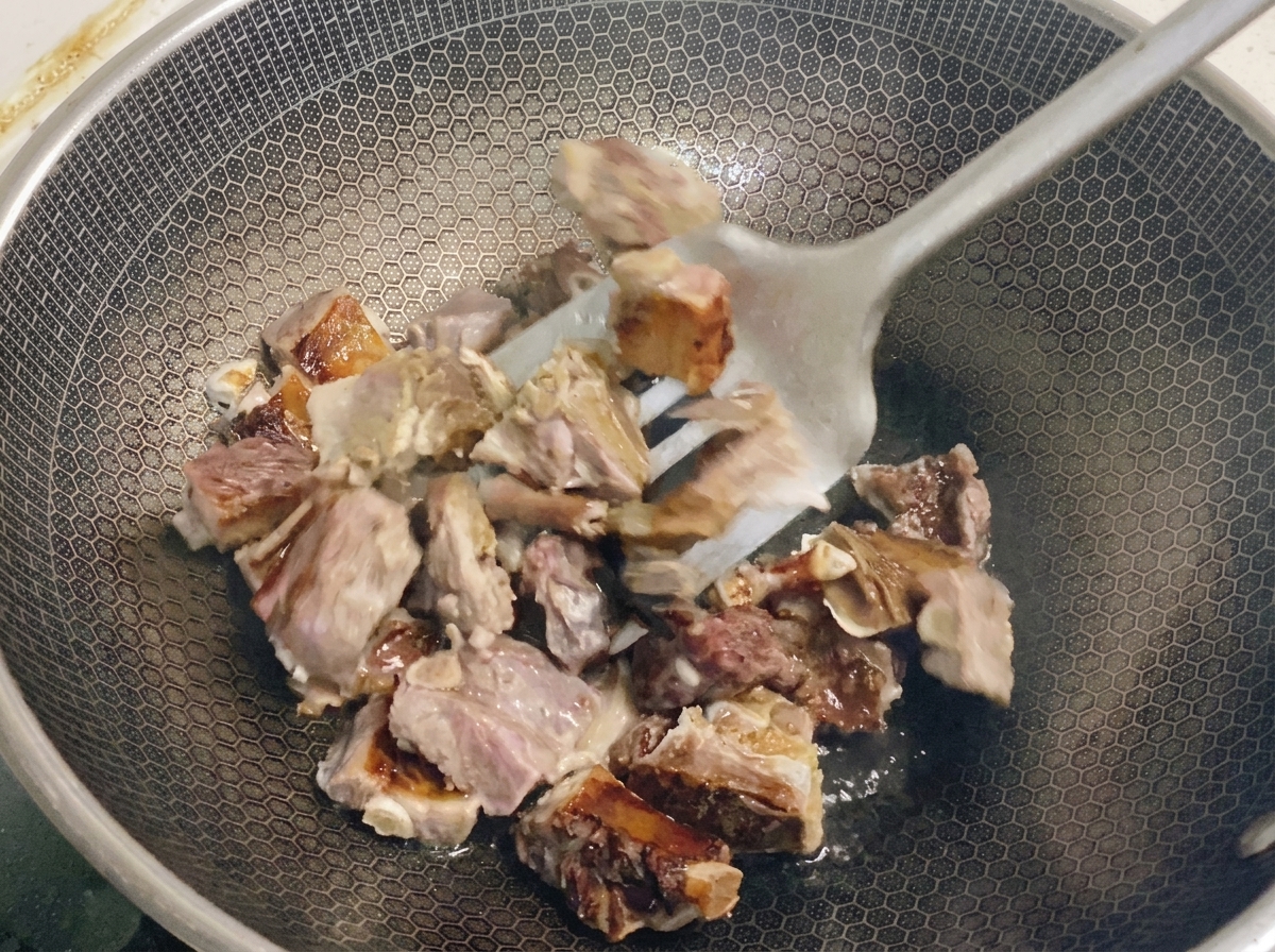 Blanchierte Rippchenstücke werden mit einem Metallwender in einem Wabenwok gewendet, um das Fett auszulassen.