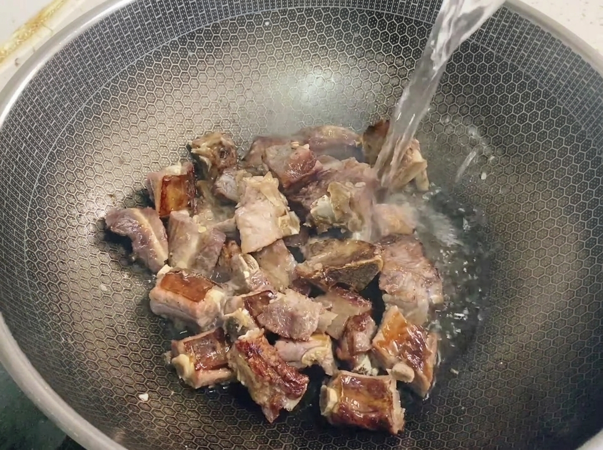 Eine klare Flüssigkeit wird über anbratende Schweinerippchen in einem Wabenwok gegossen.