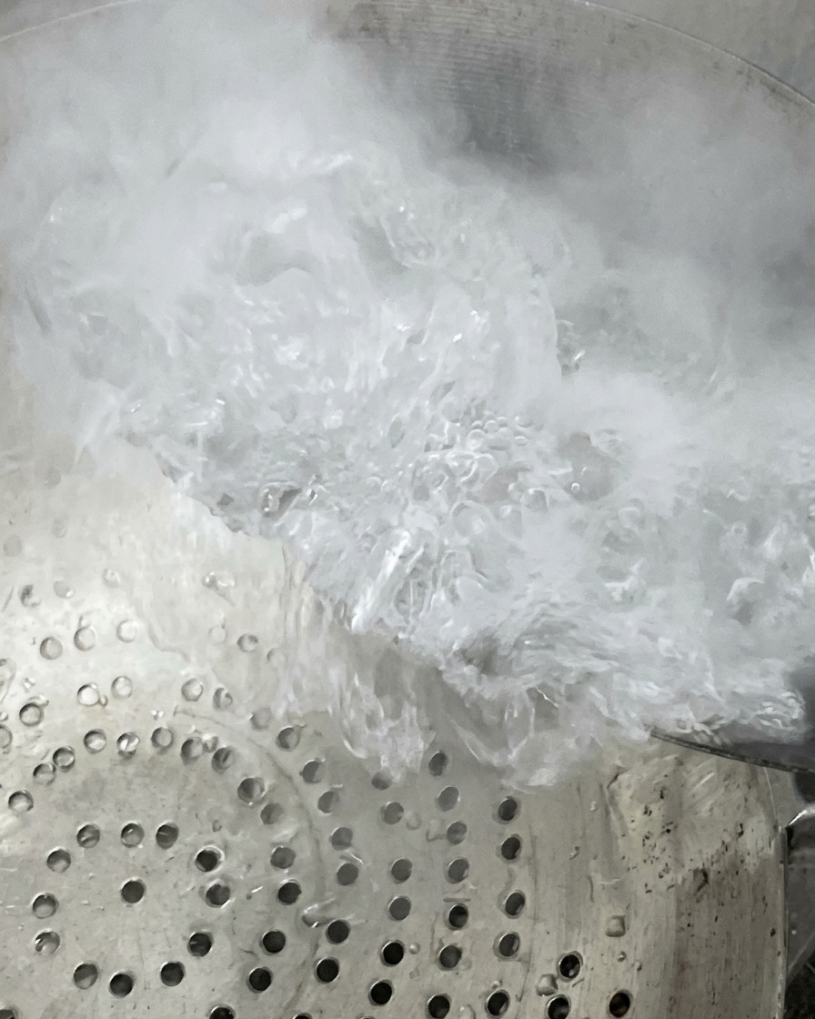 Kochendes Wasser und Dampf steigen auf, während der Inhalt über ein Metallsieb abgegossen wird.
