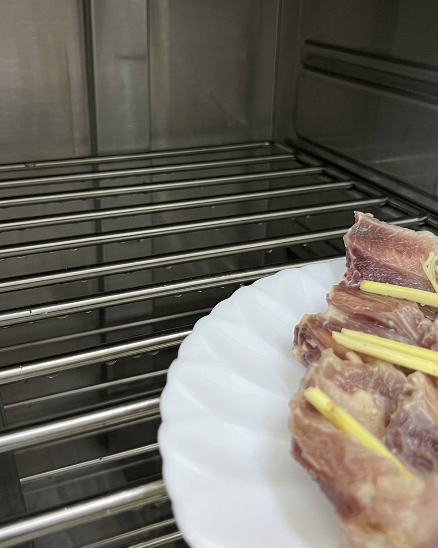 Ein weißer Teller mit Schweinerippchen und Ingwerstreifen steht auf einem Gitterrohr in einem Dampfgarer.