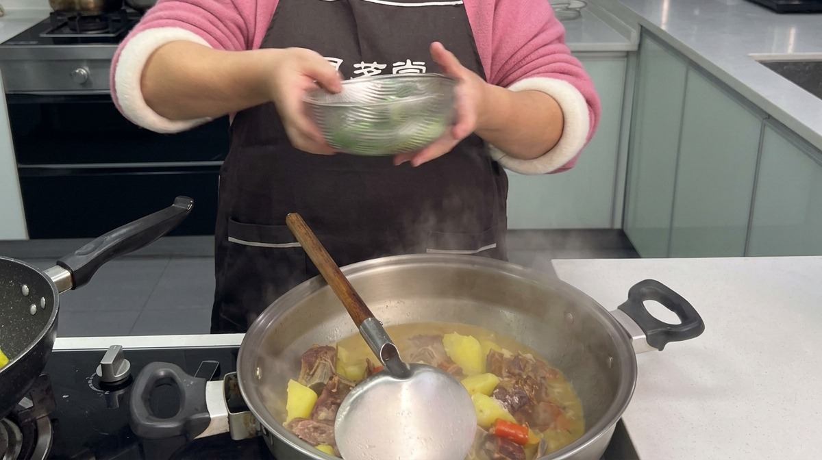 Gehackte grüne Knoblauchsprossen werden aus einer Glasschüssel in einen dampfenden Wok mit geschmorten Rippchen und Kartoffelstücken gegeben.