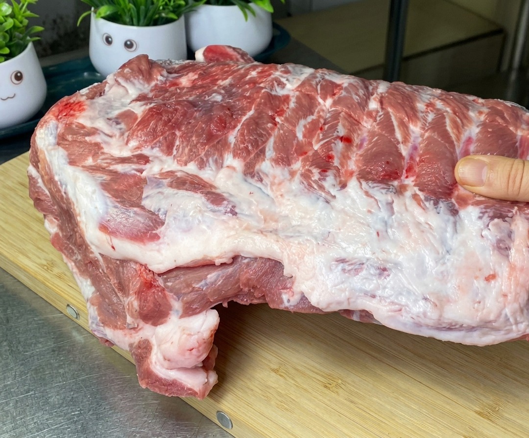 Eine große Platte roher Schweinerippchen auf einem Holzschneidebrett, mit ersten Schnitten zwischen den Knochen.