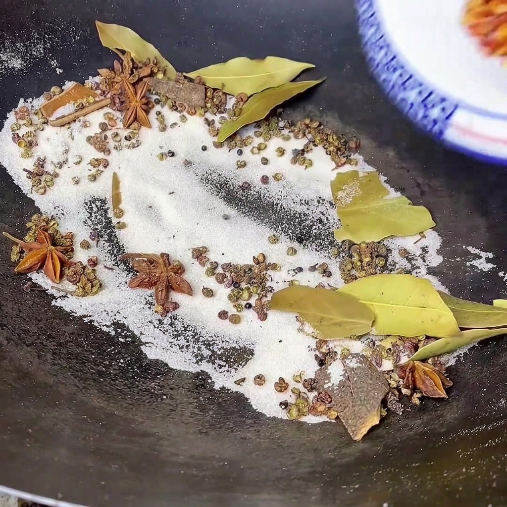 Rotes Chilipulver wird aus einer Schale in einen Wok gegossen, der geröstetes Salz, Lorbeerblätter, Sternanis und andere ganze Gewürze enthält.