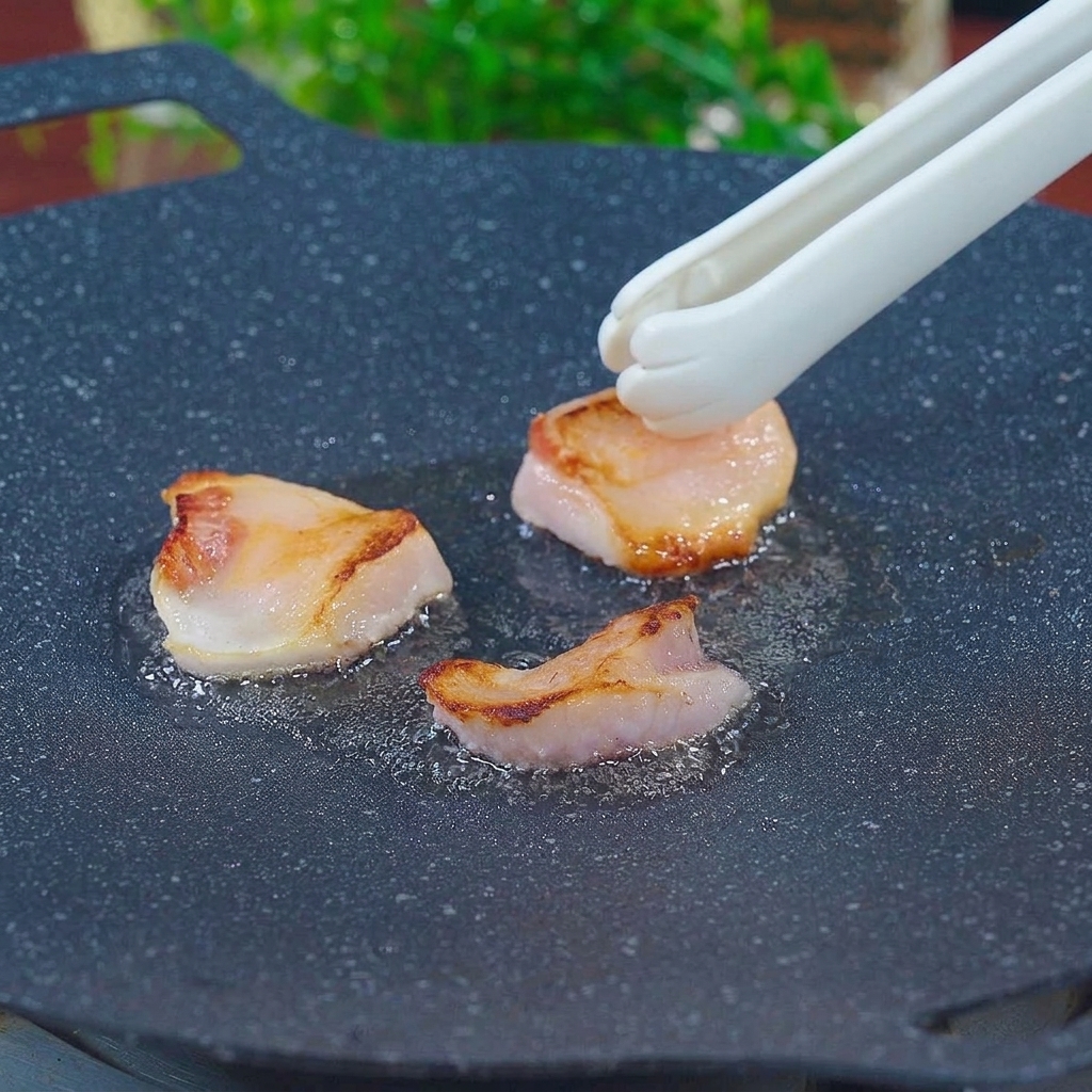 Weiße Grillzange reibt Speckstücke über eine heiße, gusseiserne schwarze Grillpfanne, um das Fett auszulassen.