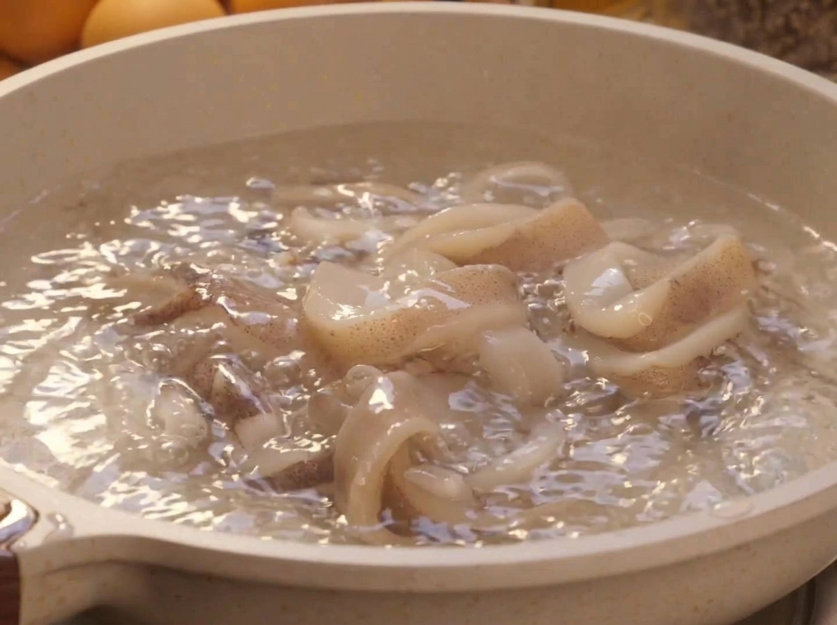 Frische weiße Tintenfischringe blanchieren in einem Topf mit sprudelnd kochendem Wasser.