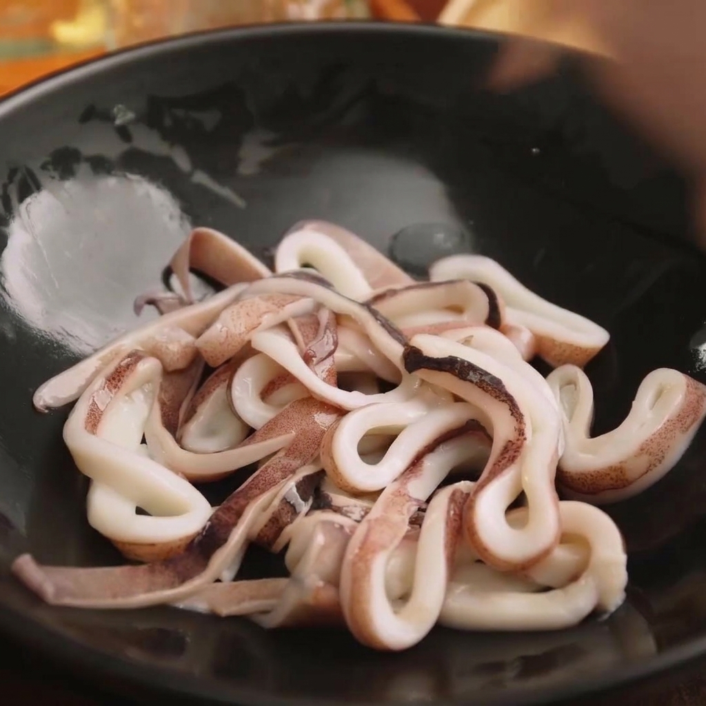 Frische Tintenfischringe liegen in einer schwarzen Schüssel bereit zum Würzen.