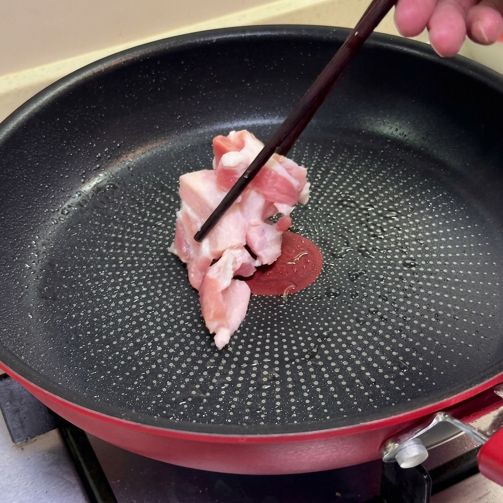 Essstäbchen legen rohe Schweinebauchscheiben in eine erhitzte, beschichtete Bratpfanne.